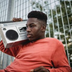 black man listening to music from retro cassette recorder outdoors